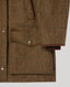 Close-up of a brown tweed jacket with a subtle windowpane plaid pattern, featuring a buttoned flap pocket and a brown ribbed knit lining visible at the cuff.