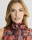 Close-up of Model wearing sleeveless silk blouse with neck tie in coral orange peacock print