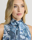 Close-up of Model wearing sleeveless silk blouse with neck tie in ice blue peacock print 
