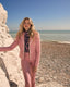 Woman in a pink suit standing on a beach with ocean and clear sky in the background