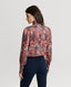 Back of Model wearing Plumage Feather Print Silk Fixed Tie Neck Blouse in Coral Red with jeans 