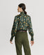 Back of Model wearing Plumage Feather Print Silk Fixed Tie Neck Blouse in green with tweed trousers 