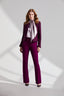 Model wearing a purple boucle jacket with purple trousers with a silk tie neck blouse on a light gray background