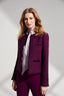 Model wearing a purple boucle jacket and pants with silk tie neck blouse on a white background