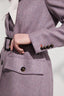 Close-up of a model wearing a purple jacket with a belt and tortoiseshell buttons on a light background