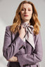 Model wearing a silk tie neck blouse underneath a purple belted jacket 