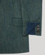 Close-up of a textured green and blue herringbone blazer fabric, showing a pocket and the cuff with three buttons and a dark blue lining.