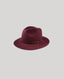 A dark burgundy felt fedora hat with a thin dark brown band and a small gold buckle, shown against a solid light gray background.