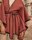 Pink cape with black trim worn by a person, standing in front of a building.