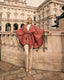 Woman in a pink cape standing in front of a historic building