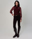 A woman modeling a burgundy ribbed mock-neck sweater with patterned sleeves, paired with dark brown pants and tall dark brown leather riding boots, against a light gray studio background.