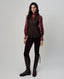 A woman modeling a dark brown vest over a long-sleeve burgundy patterned shirt, paired with dark pants and tall dark brown leather riding boots, against a light gray studio background.