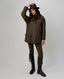 A model wearing a brown tweed field jacket with a dark burgundy collar, olive green trousers, dark brown leather riding boots, and a matching dark burgundy fedora hat, posed against a light gray studio background.
