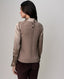 A woman shown from the back wearing a taupe knit sweater vest over a champagne satin long-sleeve blouse, paired with dark brown pants, against a neutral light gray background.