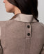 Close-up back view of a woman wearing a taupe knit sweater vest with a satin collar and two dark buttons.
