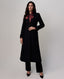 A woman models a long black coat with a double-breasted front, paired with matching black trousers, a red patterned silk neck scarf, and black pointed-toe heels against a light gray studio background.