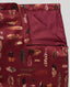 A close-up of a folded burgundy silk fabric skirt, featuring an all-over pattern of multicolored feathers in brown, black, white, and orange. The fabric is shown with one corner folded over to reveal the smooth satin reverse side.