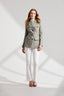 Model wearing Sage Green Safari Jacket with tortoiseshell buttons and belt buckle with white trousers and silk blouse 
