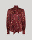A long-sleeve silk blouse in deep burgundy with an all-over feather and text print, featuring a high collar and a self-tie neck, shown against a solid light gray background.