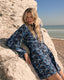 Woman in a blue butterfly dress sitting on a rock by the beach