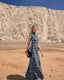 Woman in a blue butterfly dress standing on a beach with white cliffs in the background