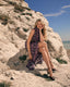 Woman in a floral dress sitting on a rocky cliff with a clear blue sky.