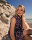 Woman in a butterfly print set sitting on a rocky beach with a clear blue sky.