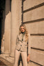 Woman in a beige suit standing against a stone building
