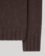 Close-up of a ribbed knit garment sleeve in a deep brown color, showing the texture and cuff detail against a light gray background.