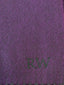A close-up of a purple woven scarf with dark green fringe and an embroidered green monogram reading 'RW', laid flat on a light wood surface.