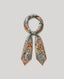 Phinda Pride silk scarf featuring an intricate botanical print with lionesses, exotic birds and tropical foliage in muted teal, blue and coral tones, finished with a burnt orange border and styled in a knotted loop.